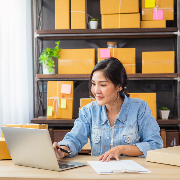 female business owner working on laptop with boxes on shelf behind her
